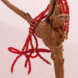 Red faceted bead necklace with golden bow pendant hanging on a natural wood branch
