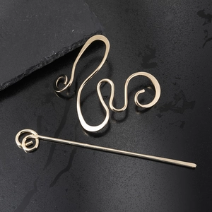 Close-up of gold irregular curved hair pin and sleek metal hair stick on black stone