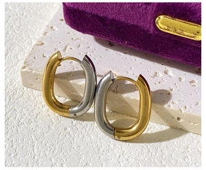 Macro view of two-tone gold and silver U-shaped earrings on a white textured stone surface