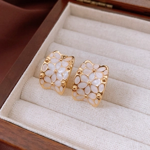 Detailed macro shot of vintage gold-plated hoop earrings with white enamel floral design