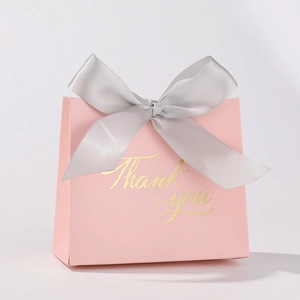 Detailed view of a pink wedding favor box with a silver ribbon and gold Thank You text