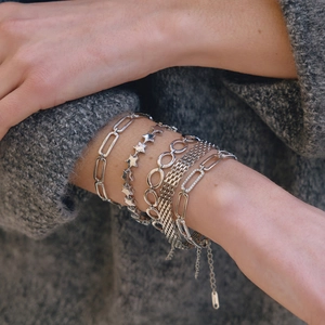 Detail of layered silver chain bracelets including star and link designs on a knit background