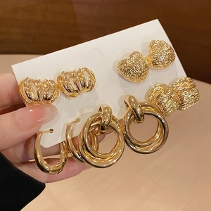 Golden earrings set with heart-shaped and geometric textured designs on a display card