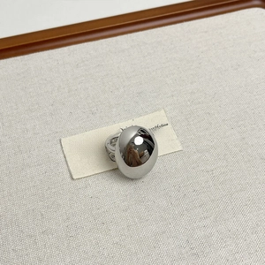 Macro view of silver egg-shaped ring with a polished mirror finish on textured fabric