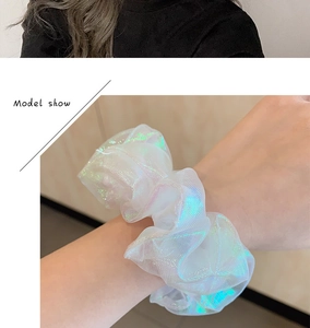 Detailed view of an iridescent white organza scrunchie worn on a model's wrist