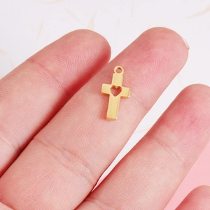 Polished gold stainless steel cross pendant with heart cutout shown on a fingertip