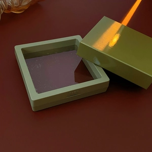 Detailed close-up of a light green square jewelry box with transparent film lid and push button