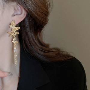 Detailed close-up of a gold butterfly tassel earring with crystal drop on a model