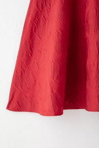 Détail de l'ourlet de la robe rouge montrant la texture plissée et le drapé du tissu