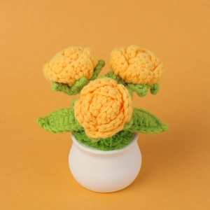 Macro shot of three crochet orange roses in a white pot with green leaves
