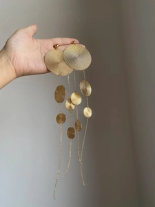 Detail view of large gold tassel earrings with textured spiral discs on metal chains