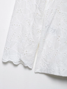 Détails de broderie complexe et bordure festonnée sur un blazer blanc en coton