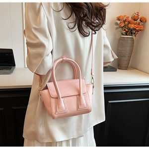 Pink bucket bag worn by model in office setting showing top handle and shoulder strap