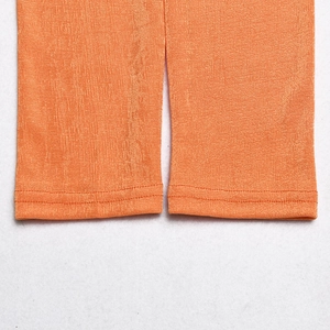 Detail of orange ribbed fabric texture and double-stitched hem on trouser legs