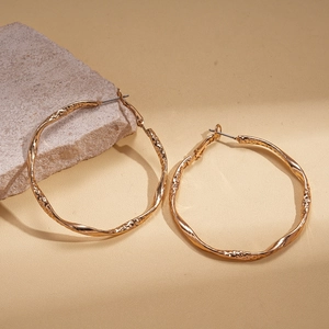 Minimalist geometric twisted gold hoop earrings placed on a natural stone background