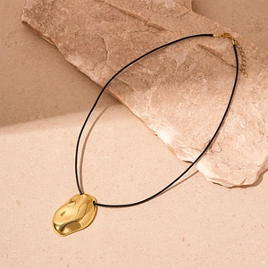 Detail of irregular gold geometric pendant on black cord over natural stone background
