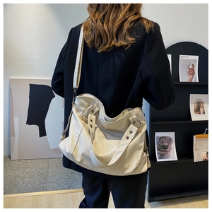 Detail of a beige oversized tote bag with rivets shown in a side-view lifestyle shot