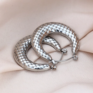 Macro shot of silver chunky hoop earrings with embossed grid pattern on champagne silk