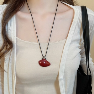 Close-up of a vintage dark red fan-shaped pendant necklace on a black string cord