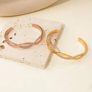 Close-up of twisted titanium steel open cuff bracelets with inlaid zircons in gold finish