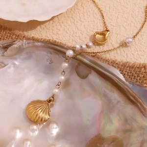 Close-up of a 18K gold plated necklace with small white pearls and shell pendant on burlap