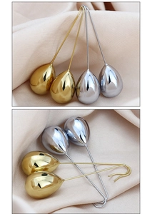 Macro detail of teardrop-shaped metal earrings in gold and silver finish on beige fabric