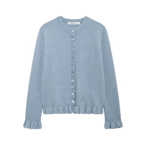 Detail of light blue knit cardigan featuring ruffled edges and pearl white button closure