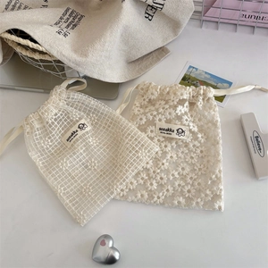 Dettaglio di sacchetti in pizzo bianco con ricamo a margherita e chiusura a coulisse