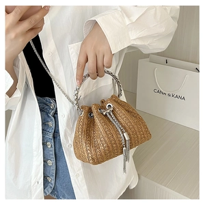Detail of straw bucket bag with silver metal ring handles and tassel chain decoration