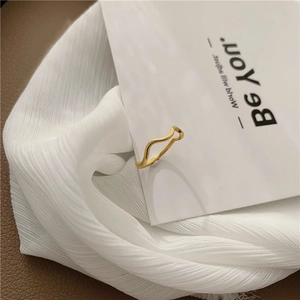 Minimalist golden wavy geometric ring displayed on an elegant white textured fabric
