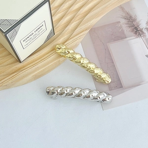 Close-up of elegant gold and silver twisted texture hair clips on a wooden tray