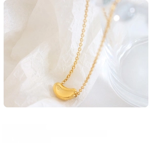 Detailed close-up of golden bean pendant on a fine metal chain over white fabric