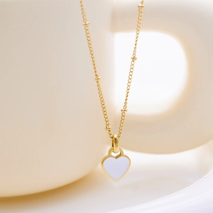 Macro shot of a gold heart pendant necklace with white enamel hanging on a ceramic cup