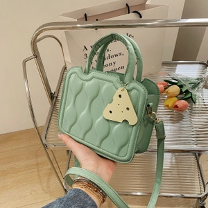 Detail of light green quilted PU bag with wavy stitching and yellow cheese charm