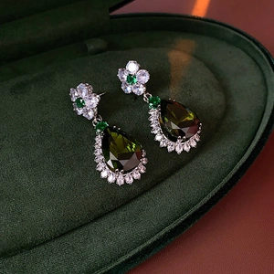 Detailed close-up of green zircon flower and teardrop earrings on a velvet box