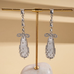 Boucles d'oreilles nœud argenté avec gouttes en résine et zircon sur présentoir