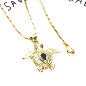 Macro shot of gold turtle pendant with teardrop green gemstone and zircon inlays