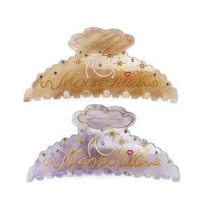 Close-up of marble-textured hair claws with Moonchild gold lettering and small rhinestones