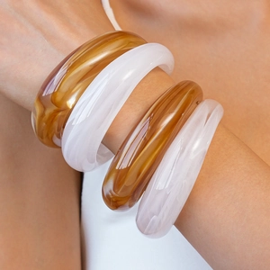 Detail of stacked acrylic cuff bracelets with amber marble and milky white textures