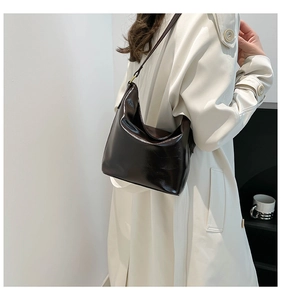 Deep brown glossy patent leather hobo bag worn on shoulder by model in a minimalist room