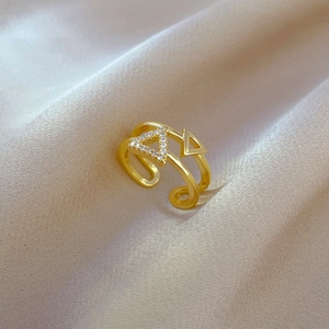 Close-up of gold geometric double-layered triangle ring with zircon stone on satin fabric