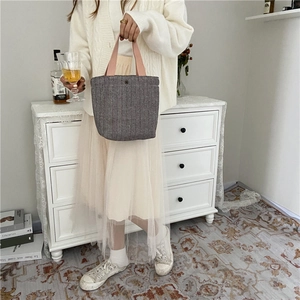 Detail of grey herringbone tote bag with pink handles held in a cozy home setting