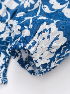 Dettaglio del ricamo floreale blu e bianco su una camicetta sciancrata con scollo a V