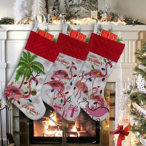 Three red and white Christmas stockings with flamingo and palm tree patterns by a fireplace