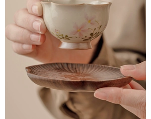 Detail of grey daisy ceramic tea cup being placed on a handcrafted wooden saucer