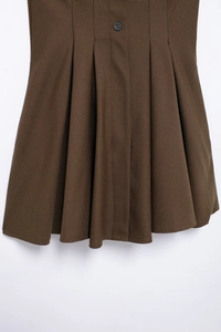 Detail of a brown houndstooth pleated mini skirt with a decorative waist button