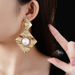 Detailed view of gold geometric drop earrings with pearl and rhinestone on model