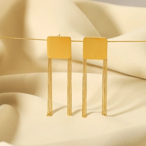 Elegant gold square tassel earrings in stainless steel on a soft beige fabric background