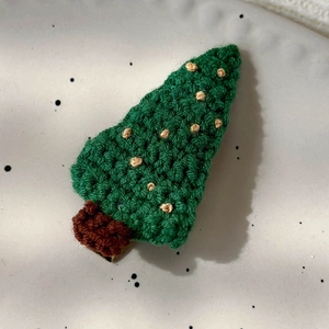 Detail of hand-knitted green Christmas tree hair clip on a spotted ceramic plate