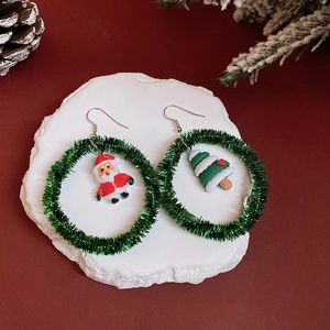Detailed view of Christmas wreath earrings with Santa Claus and tree charms on a festive background